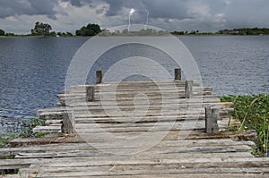 Empty wooden bridge over pond with lightning background