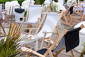 Empty wooden deck chairs near the cafe in summer. Tables and deckchairs at sidewalk cafe. Touristic setting, cafe table, sidewalk