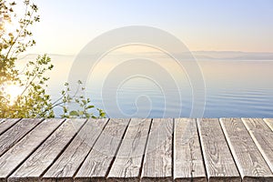 An empty wooden deck or table against the backdrop of a calm morning lake at dawn in pastel colors. Product display frame