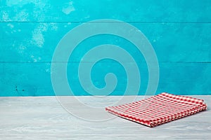 Empty wooden deck table with checked red tablecloth over rustic blue background. Summer concept