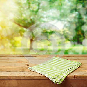 Empty wooden deck table with checked tablecloth over green park bokeh background for product montage
