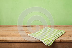 Empty wooden deck table with checked tablecloth over green wall background