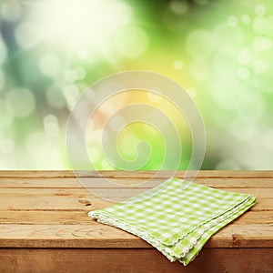Empty wooden deck table with checked tablecloth over nature bokeh background for product montage