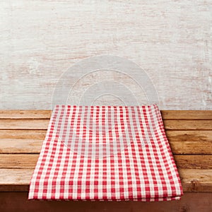 Empty wooden deck table with checked tablecloth over rustic wall.