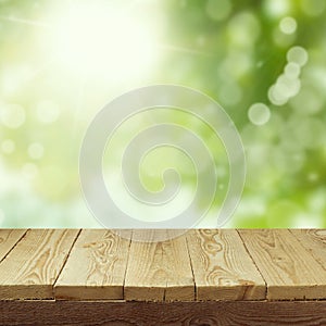 Empty wooden deck table with foliage bokeh background for product display montage. Spring or summer