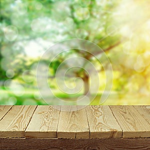 Empty wooden deck table with foliage bokeh background for product display montage. Spring or summer