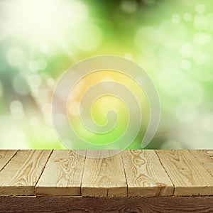 Empty wooden deck table with foliage bokeh background for product display montage. Spring or summer