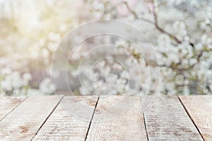 Empty wooden deck table with foliage and white blossoming tree bokeh background, copy space for product display