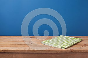 Empty wooden deck table with green checked tablecloth over blue wall background