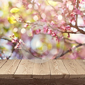 Empty wooden deck table over blooming tree bokeh background for product montage display.
