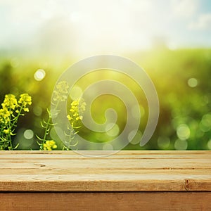 Empty wooden deck table over green meadow bokeh background for product montage display. Spring or summer season