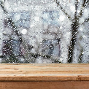 Empty wooden deck table over wet glass window. Rainy weather concept.