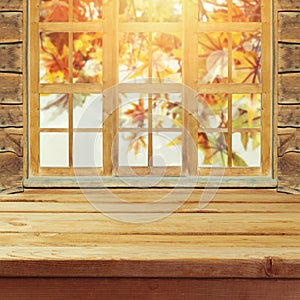 Empty wooden deck table over wndow and autumn leaves bokeh background