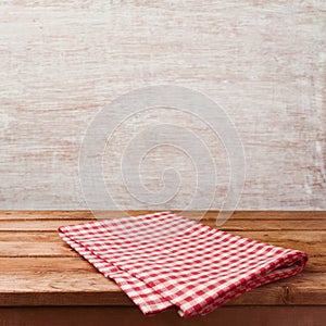 Empty wooden deck table with red checked tablecloth over rustic wall background for product montage display.