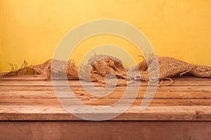 Empty wooden deck table and sackcloth over yellow wall background for product montage