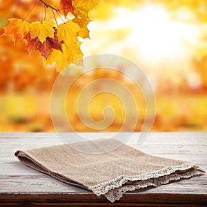 Empty wooden deck table with tablecloth over bokeh autumn leaves background