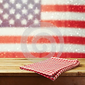 Empty wooden deck table with tablecloth over USA flag bokeh background. 4th of July celebration picnic background.