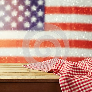 Empty wooden deck table with tablecloth over USA flag bokeh background. 4th of July celebration picnic background.