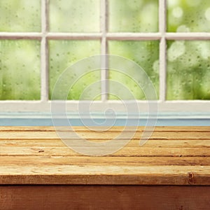 Empty wooden deck table and window with rain drops