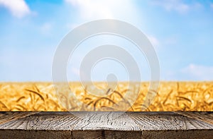 Empty wooden desk with empty space for product display over golden agricultural wheat field and blue sky.
