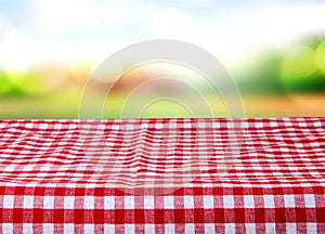 Empty wooden desk table with red checkered tablecloth over abstract bright light green spring or summer background. Template for