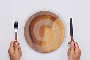 Empty wooden dish with knife and fork in hands. Top view