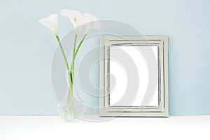 Empty wooden frame and flowers in vase on table on blue background. mock up