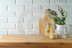 Empty wooden l table with plant, food jars and cutting board over white brick wall background. Kitchen mock up for design and