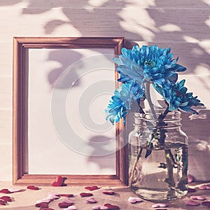 Empty wooden photo frame, blue chrysanthemums in vases, shapes in the form of hearts are on a light wooden background.