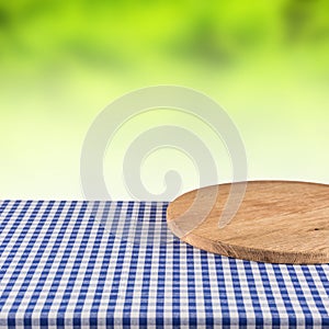 Empty wooden pizza board on blue checkered tablecloth.