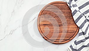 Empty wooden pizza platter with napkin set up on marble stone kitchen table. Pizza board and tablecloth on white marble background