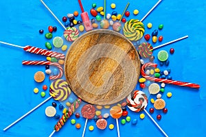 Empty wooden plate and frame of colored lollipops,sweets, candy on a light blue background. Children`s holiday. Top view, flat la