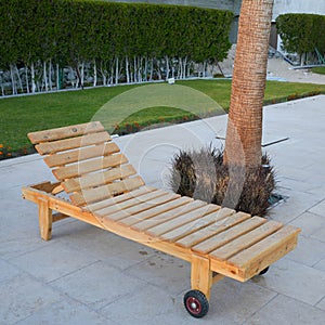 Empty wooden sunbed deck chair on tiles in a garden with grass