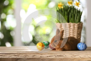 Empty wooden surface and wicker basket with flowers, furry bunny and colorful Easter eggs on background