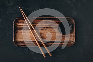 Empty wooden sushi plate with chopsticks on dark black stone background