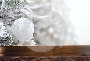 Empty wooden table on the background of background of a snowy decorated Christmas tree branch with white ball. Christmas