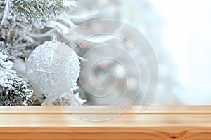 Empty wooden table on the background of a snowy decorated Christmas tree branch with white ball. Christmas background. Ready for
