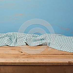 Empty wooden table with checked blue tablecloth over rustic painted wall