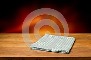 Empty wooden table with checked tablecloth over blur fire background. photo