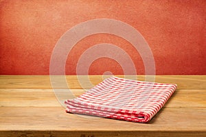 Empty wooden table with checked tablecloth over grunge red concrete wall.