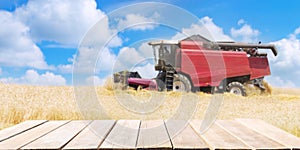 empty wooden table and combine harvester working in wheat field in a summer day photo