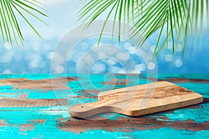 Empty wooden table with cutting board over tropical beach with palm leaves bokeh background. Summer mock up for design and
