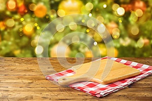Empty wooden table with cutting board and tablecloth over Christmas tree bokeh background. Holiday product montage display or mock