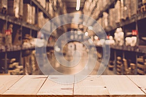 Empty wooden table on defocuced blurred boxes on rows of shelves