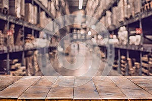 Empty wooden table on defocused blurred boxes on rows of shelves