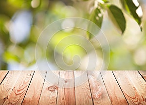 Empty wooden table with foliage bokeh background.