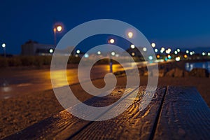 Empty wooden table lighten up by warm city lights. Empty road out of focus. Blue cloudy sky in the background. Night out of