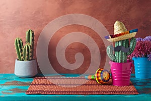 Empty wooden table with place mat and cactus decoration over wall background. Mexican party mock up for design and product