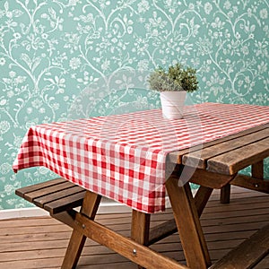 Empty wooden deck table and red checked tablecloth over mint wallpaper background
