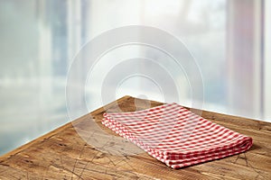 Empty wooden table with red checked tablecloth over  blurred window background.  Kitchen mock up for design and product display